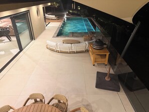 Un área de piscina moderna al aire libre con una tumbona, una mesa redonda y sillas de mimbre.