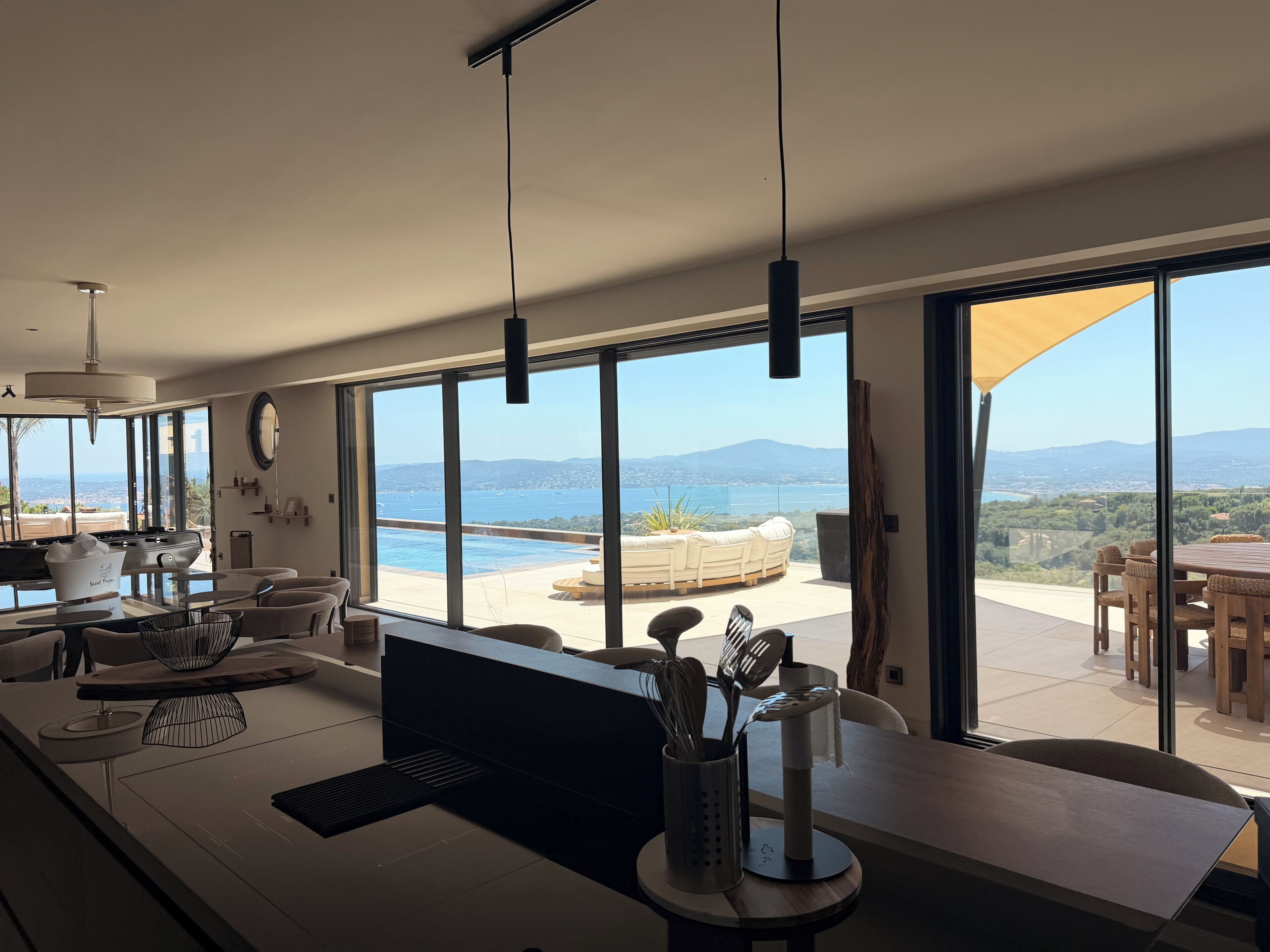 A modern kitchen with a large island, a dining area with a view, and a poolside seating area.