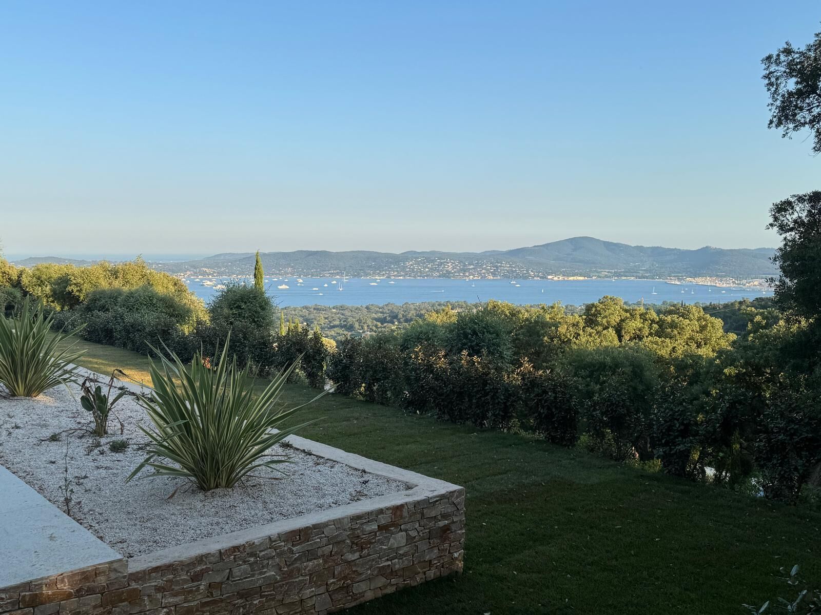 Un giardino curato con vista su una cittadina costiera e montagne sullo sfondo.