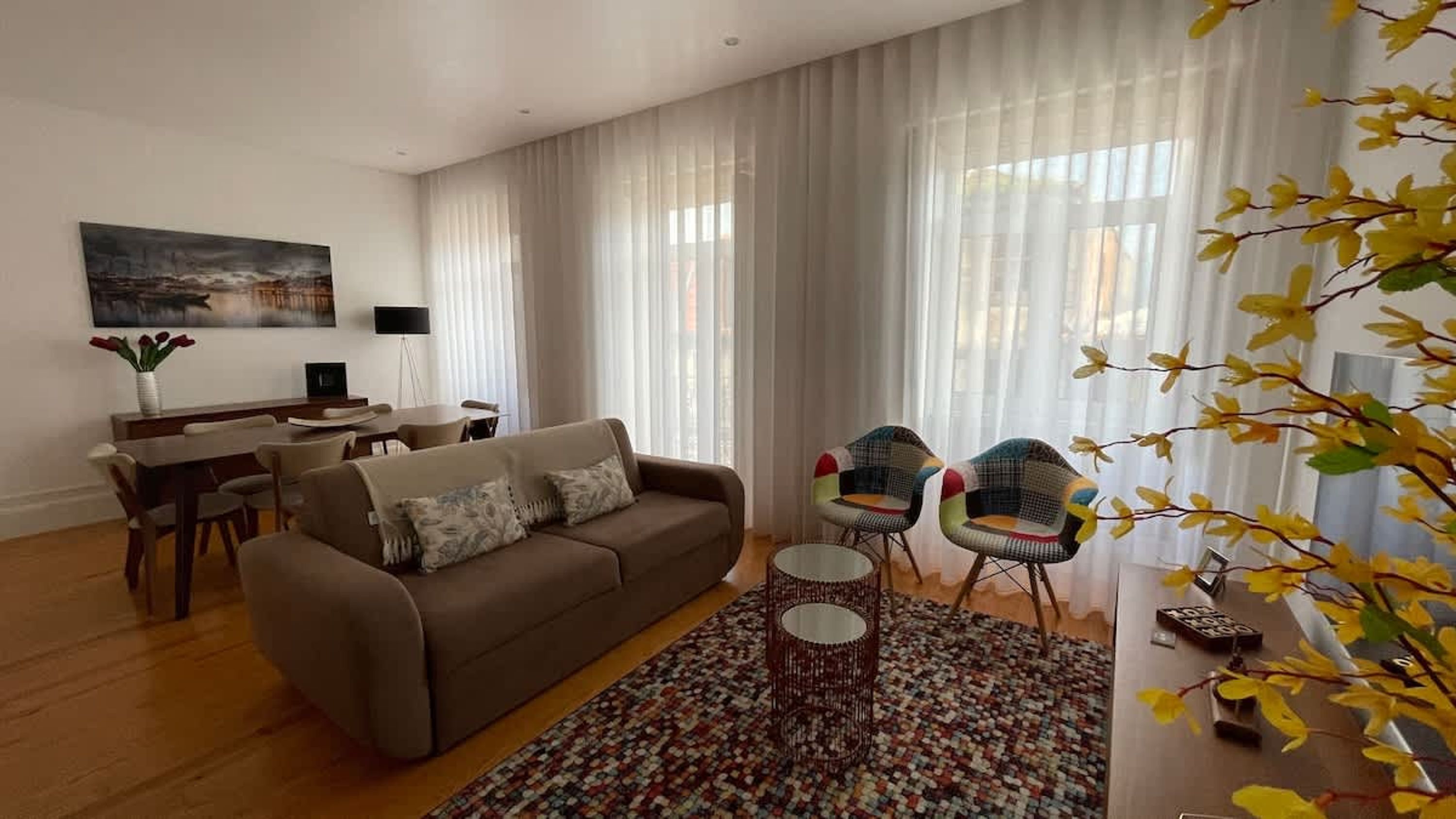 A living room with a sofa, two chairs, a coffee table, a painting, and a dining area.