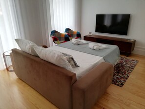 A modern bedroom with a sofa bed, a TV, a bedside table, and a patterned rug. - Downtown Apartment Porto by Liiiving (Porto)