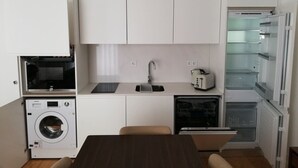A compact kitchen with a washing machine, a microwave, a toaster, and a refrigerator. - Downtown Apartment Porto by Liiiving (Porto)