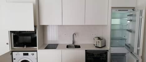 Une cuisine compacte équipée d’un lave-linge, d’un four à micro-ondes, d’un grille-pain et d’un réfrigérateur.