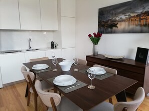 Ein Essbereich mit einem dunklen Holztisch, gedecktem Platz für vier Personen, weißen Tellern und Gläsern, sowie einem kleinen Beistelltisch mit einer Vase roter Blumen.