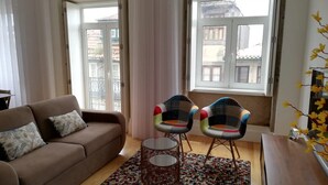 A living room with a sofa, two chairs, a small table, a patterned rug, and a window with a view. - Downtown Apartment Porto by Liiiving (Porto)