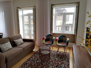 A living room with a sofa, two chairs, a small table, a patterned rug, and a window with a view. - Downtown Apartment Porto by Liiiving (Porto)