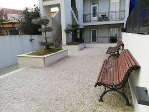 A courtyard with a paved area, two wooden benches, and a small garden with a tree. - Downtown Apartment Porto by Liiiving (Porto)