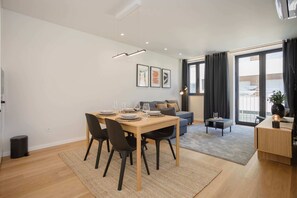 Ein moderner Essbereich mit einem Holztisch, schwarzen Stühlen und einer grauen Couch im Hintergrund.