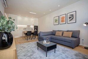 A modern living room with a grey sofa, a coffee table, and a dining area with chairs and a table. - Liiiving in Matosinhos - Mercatus Apartment D (Matosinhos)