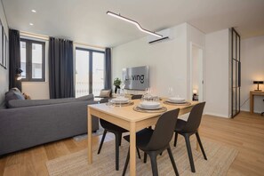 A modern living room with a sofa, dining table set for four, and a TV mounted on the wall. - Liiiving in Matosinhos - Mercatus Apartment D (Matosinhos)