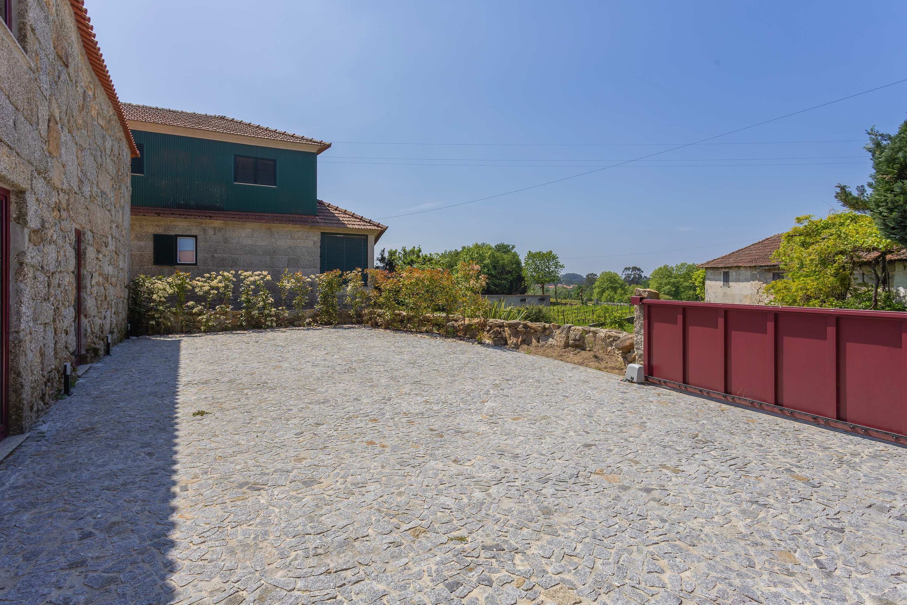 Un patio de piedra con suelo adoquinado, un edificio verde con tejado de tejas y una cerca roja.