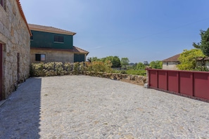 A stone courtyard with a cobblestone floor, a green building with a tiled roof, and a red fence.