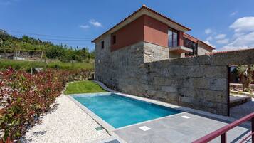 A two-story stone house with a swimming pool, surrounded by a garden and a stone wall.