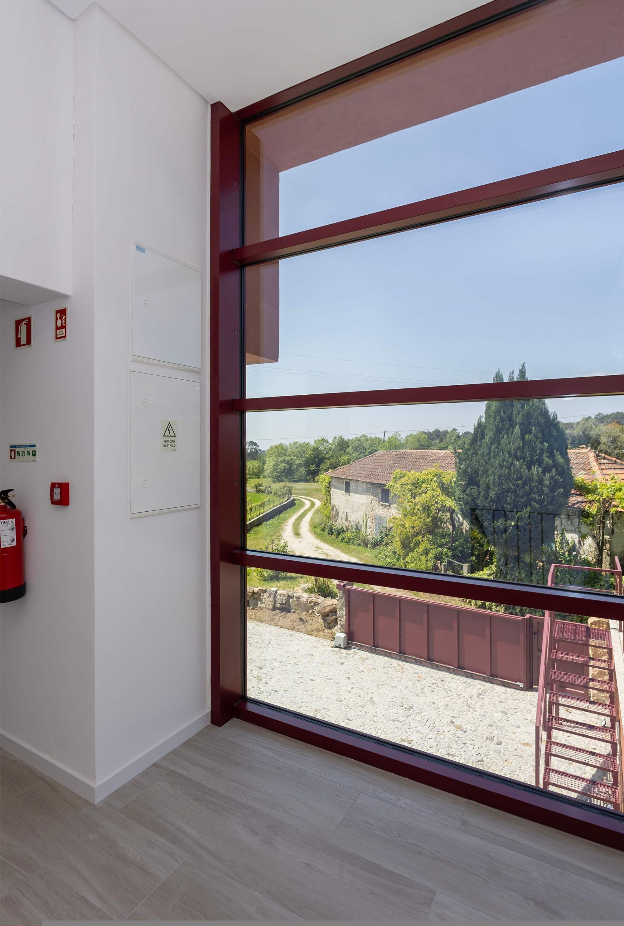 A room with a large window, a fire extinguisher, and emergency exit signs on the wall.