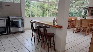 Uma cozinha com fogão, banquetas de bar e cadeiras de madeira.