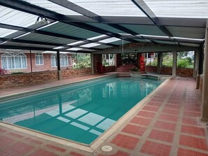 An indoor swimming pool with a tiled floor, a covered roof, and brick walls.