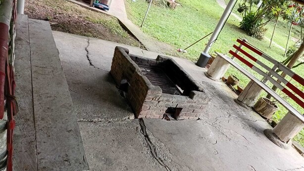 A concrete outdoor area with a brick structure, possibly a barbecue or grill, and a metal fence.