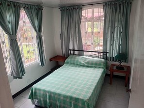Une chambre à coucher avec un lit, une table de chevet, une fenêtre avec des rideaux et une vue sur l’extérieur.