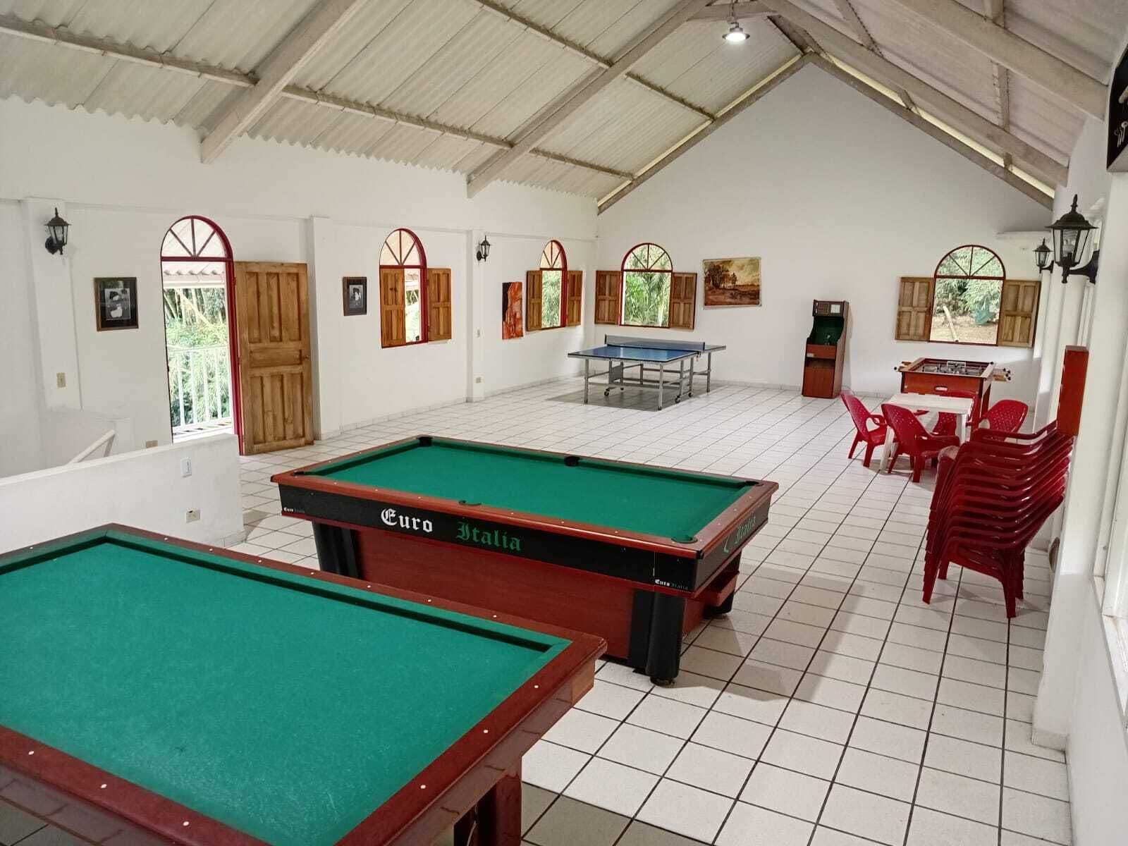 A billiards room with two pool tables, a foosball table, and red plastic chairs.