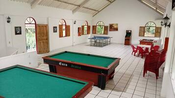A billiards room with two pool tables, a foosball table, and red plastic chairs.
