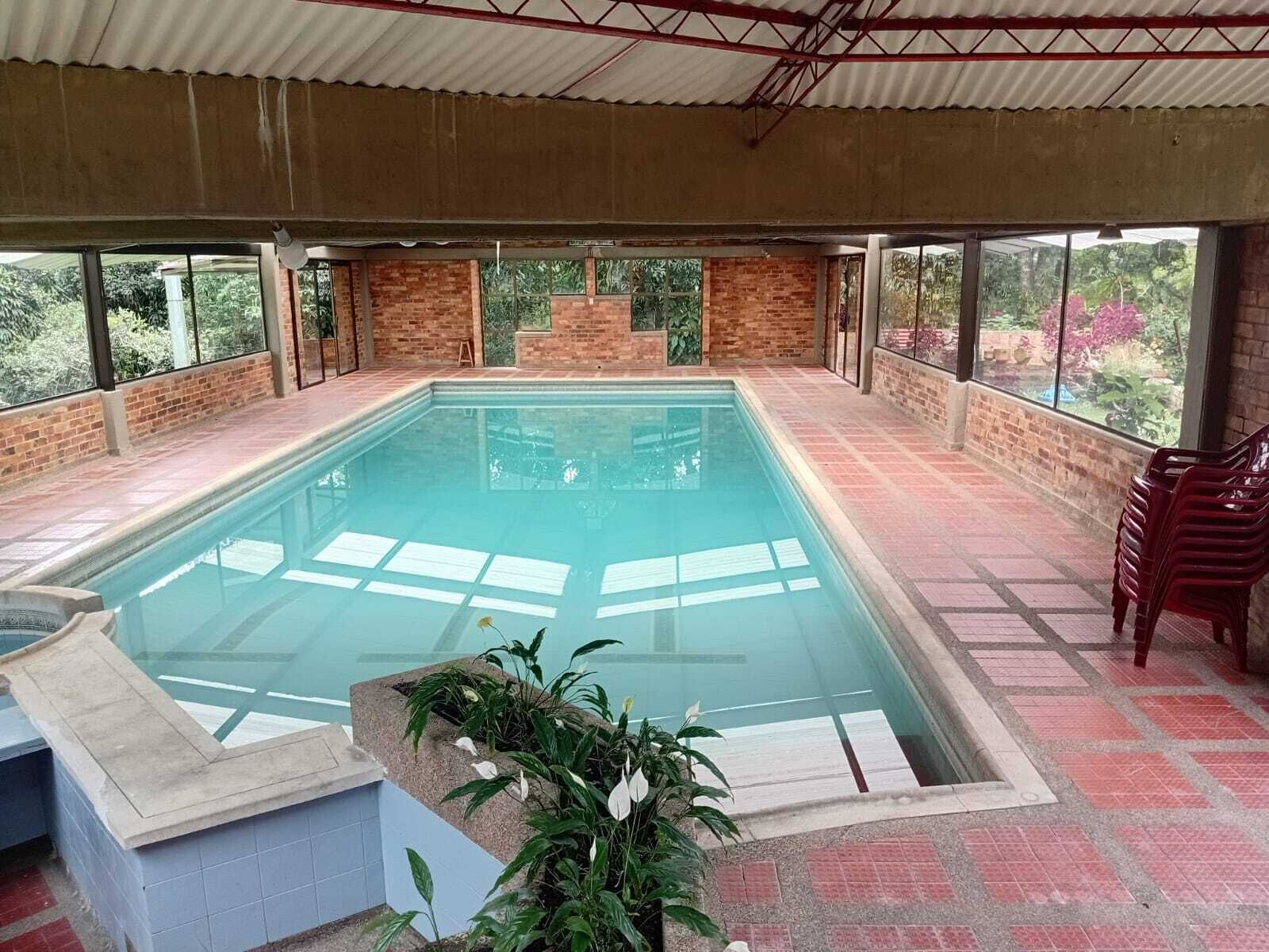 Une piscine intérieure avec un sol carrelé, entourée de murs en briques et dotée de grandes fenêtres.