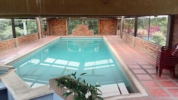 Une piscine intérieure avec un sol carrelé, entourée de murs en briques et dotée de grandes fenêtres.