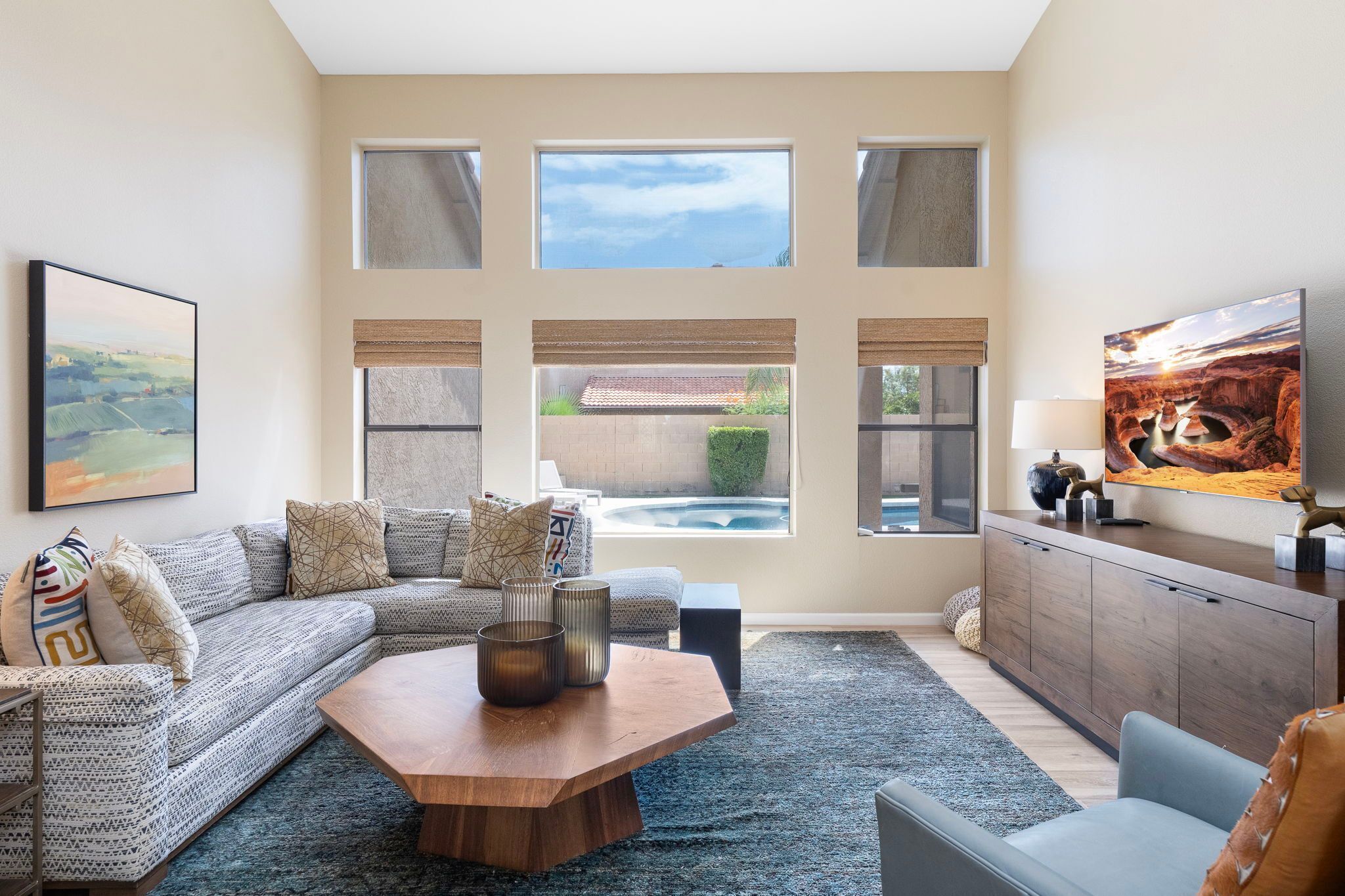 A living room with a sectional sofa, a coffee table, a TV, and a view of a swimming pool.