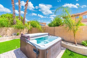 Un jacuzzi dans un jardin, avec un mur en briques, de l’herbe verte et des palmiers.