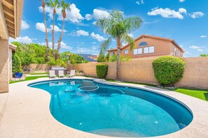 A swimming pool with a curved design, surrounded by a brick wall, palm trees, and a house in the background. - Desert Retreat with Pool Near Golf & Hiking (Scottsdale)