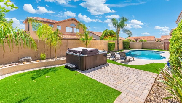 Un jardin avec un jacuzzi, une piscine, une pelouse artificielle et une terrasse en briques.