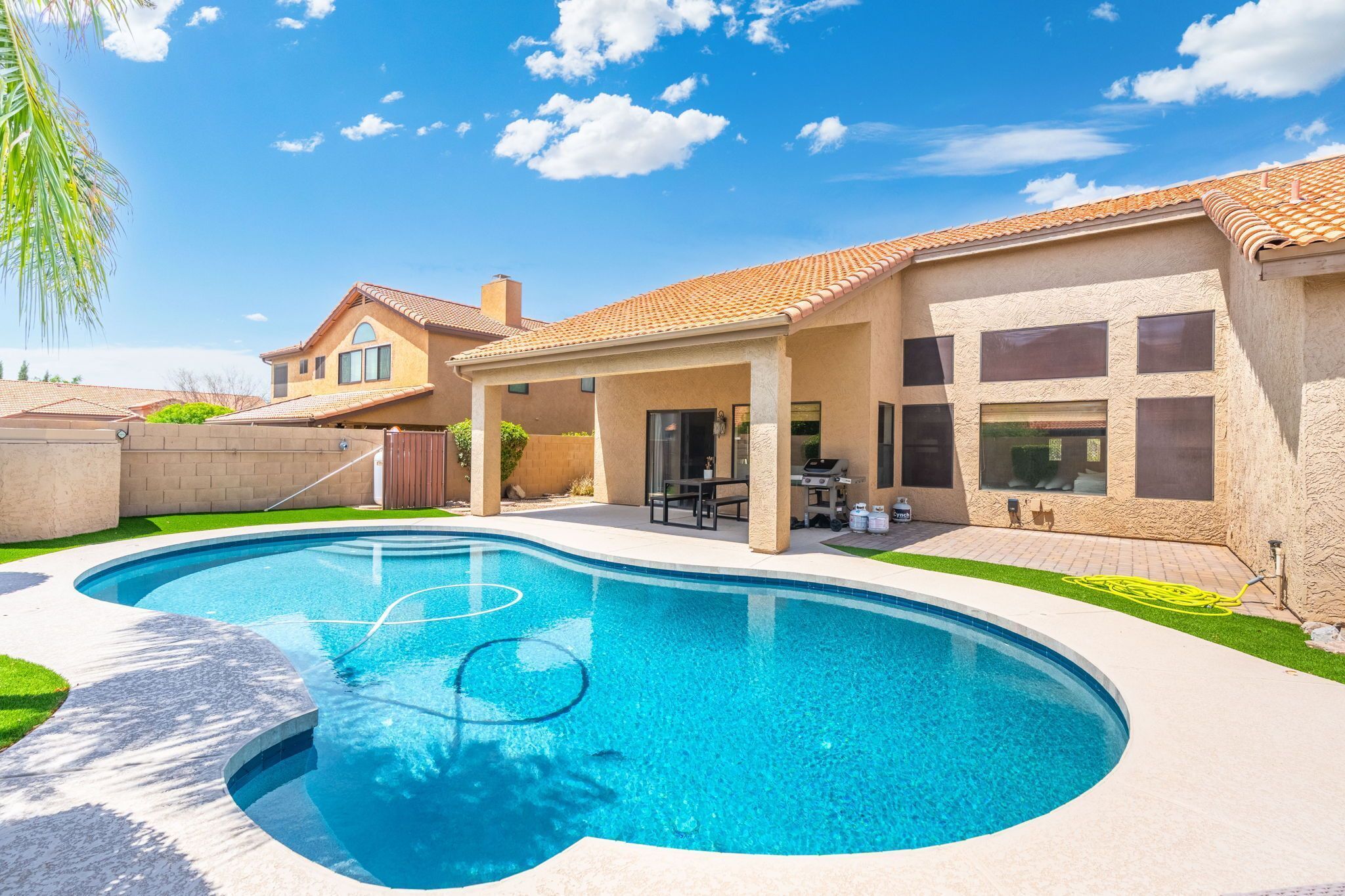 En baghave med swimmingpool, terrasse og et hus med tegltag.