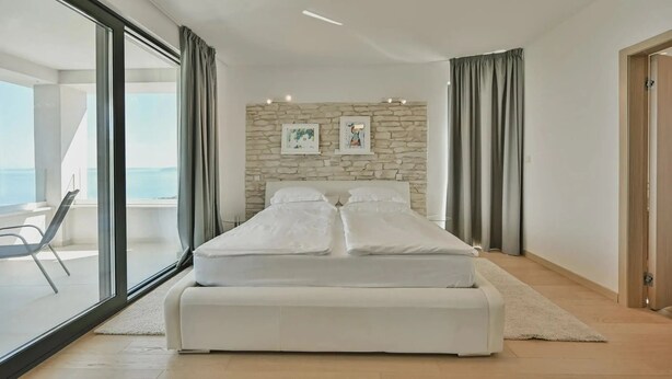 A modern bedroom with a large bed, a stone wall, and a balcony with a view. - Villa Maremont Nearby Opatija - Crovillas (Opatija)