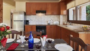 A kitchen with wooden cabinets, a refrigerator, a dishwasher, and a window with a view. - Villa Petra Sun-Coral Bay (PAFOS)