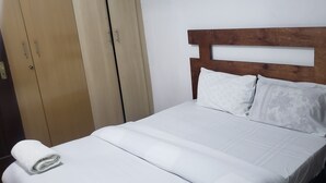 A bed with white bedding, a wooden headboard, and two pillows. A rolled white towel is placed at the foot of the bed. - Cozy 1-bedroom apartment with AC in pleasant Machakos (Machakos)