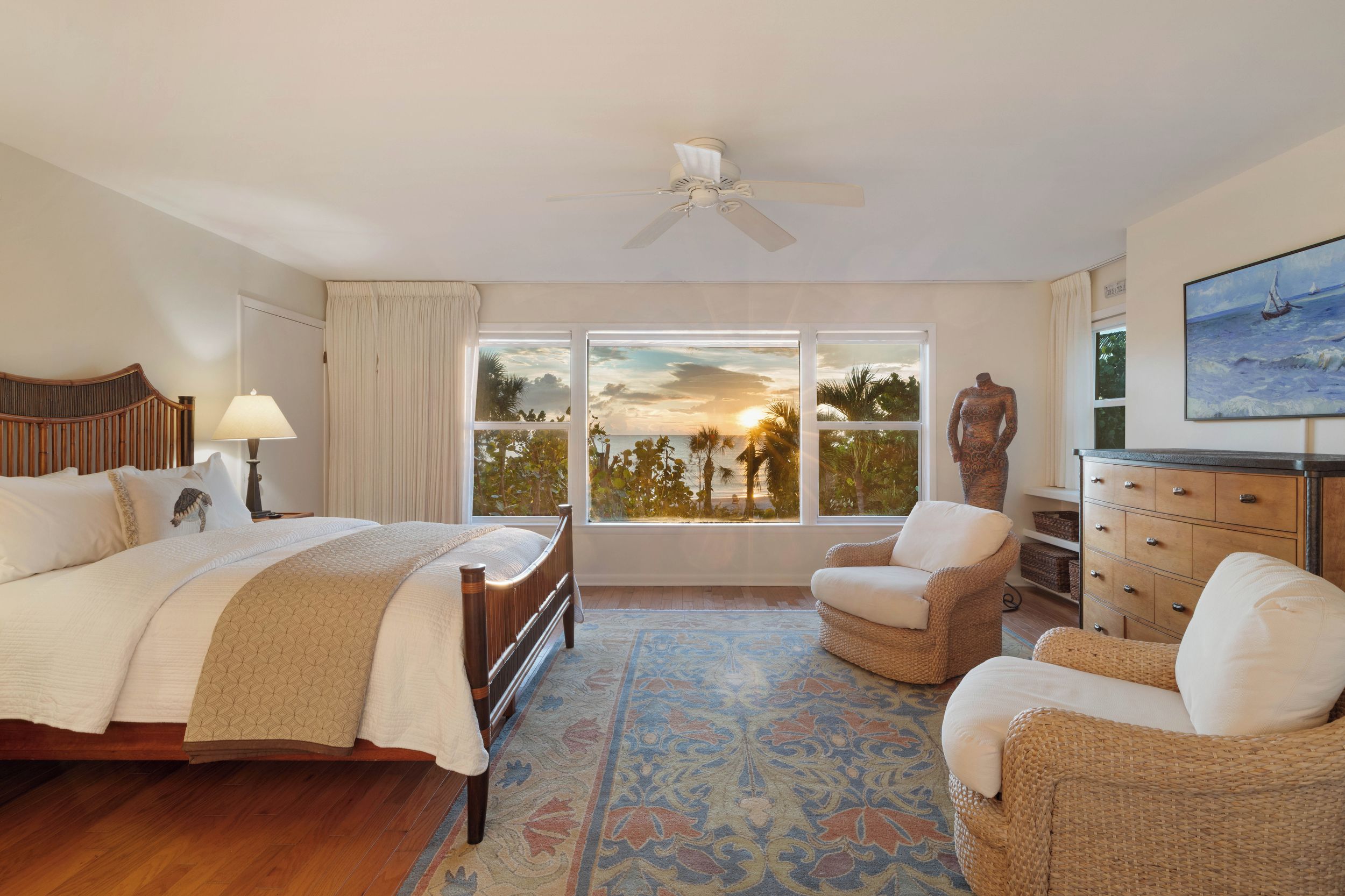 A bedroom with a bed, two chairs, a dresser, a ceiling fan, and a painting of a sailboat.