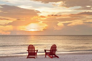Two red Adirondack chairs facing a sunset over the ocean. - The Original Beach House: A Timeless Gulf-Front Retreat on Siesta Key Beach (Sarasota)