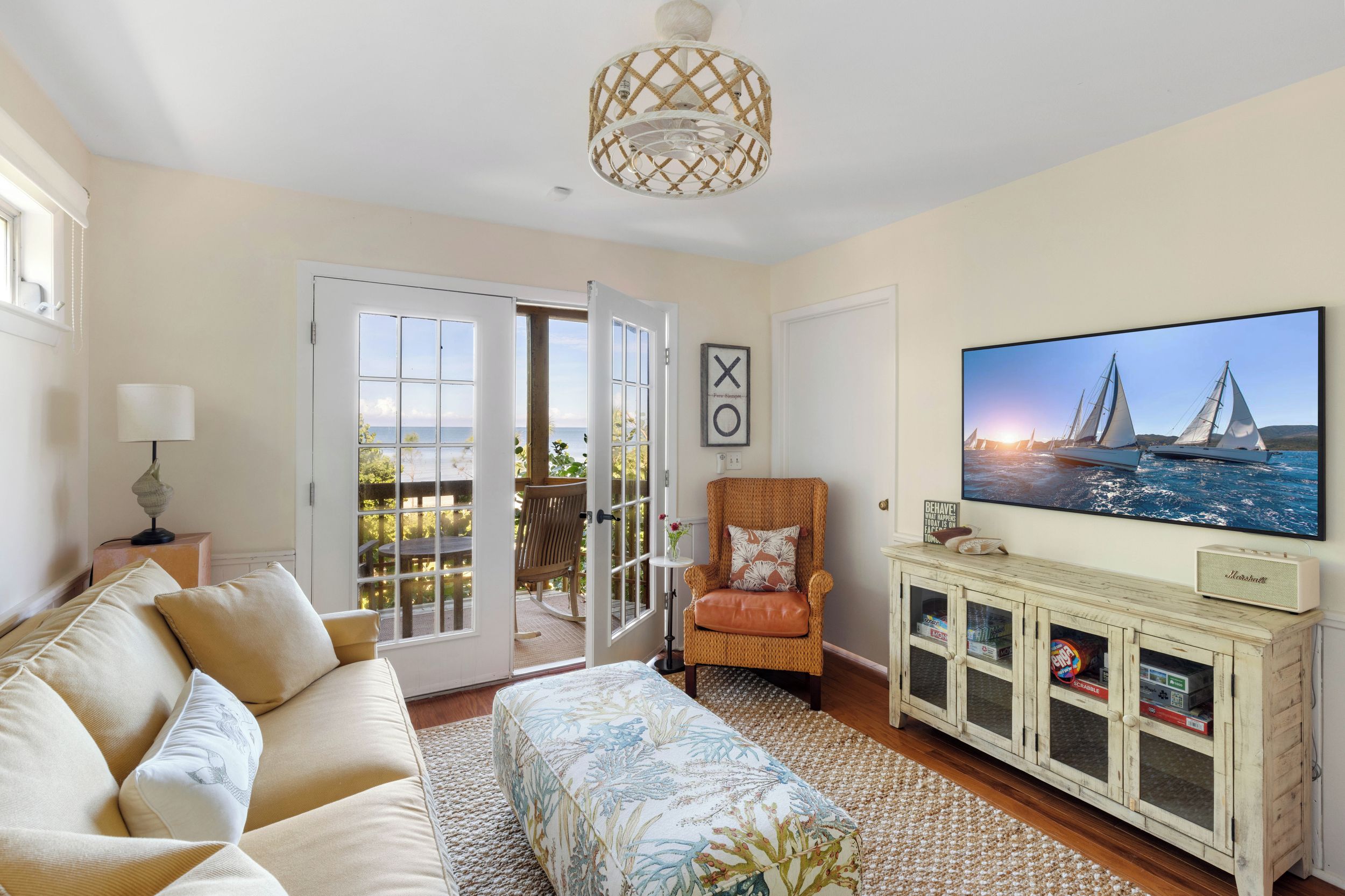 Una sala de estar con sofá, televisión, sillón de mimbre y un mueble con cajas de almacenamiento.