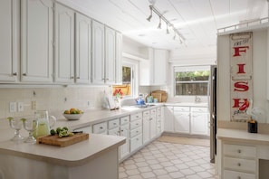 A kitchen with white cabinets, a tiled backsplash, a sink, and a decorative sign. - The Original Beach House: A Timeless Gulf-Front Retreat on Siesta Key Beach (Sarasota)