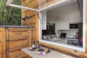 Una cabaña de madera con un cerramiento de vidrio corredizo que da a una cocina con armarios blancos, un microondas y un fregadero.