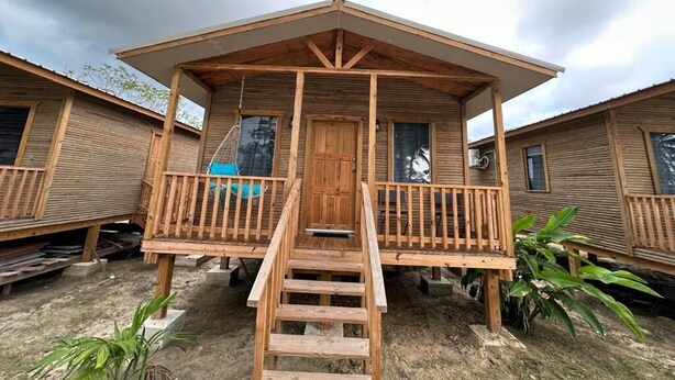 A wooden cabin with a porch, a staircase leading to the entrance, and a small garden area.