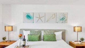 A hotel room with a bed, two nightstands, a lamp, a wine bottle, and a vase with flowers. - New! Marina Panorama 2BR - Bay View Fitness Center (Hallandale Beach)
