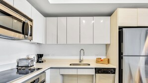 A modern kitchen with white cabinets, stainless steel appliances, a dishwasher, and a coffee maker. - New! Marina Panorama 2BR - Bay View Fitness Center (Hallandale Beach)