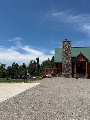 Une cabane en rondins avec une cheminée en pierre, une terrasse en bois et une allée gravillonnée.