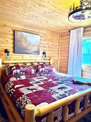 Une chambre dans une cabane en bois, avec un lit, un tableau et un ventilateur de plafond.