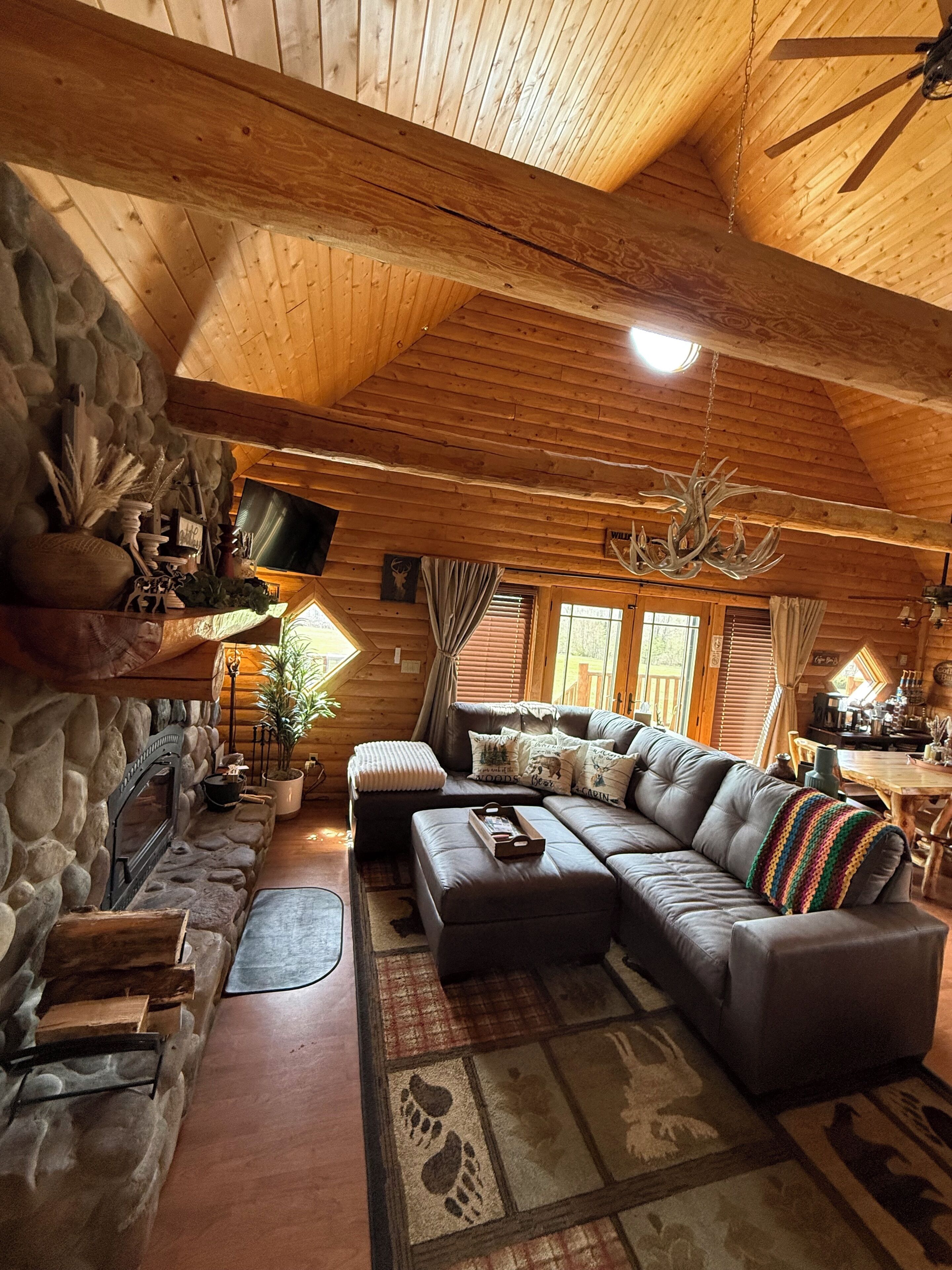 Ein gemütliches Blockhaus-Interieur mit Kamin aus Stein, einer großen Ledersofa und einer Holzbalkendecke.