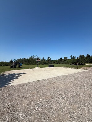 Une zone en béton comprenant une aire de jeux et un panier de basketball.