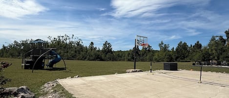 Una cancha de baloncesto de concreto con un aro, rodeada de césped y árboles.