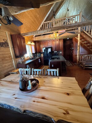 A log cabin interior with a wooden dining table, kitchen area, and a staircase leading to a loft. - Family friendly 3-bedroom cabin in peaceful Vanderbilt. Private. Large groups. (Vanderbilt)