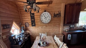 A wooden dining table with chairs, a clock, and a ceiling fan in a cabin-style room. - Family friendly 3-bedroom cabin in peaceful Vanderbilt. Private. Large groups. (Vanderbilt)