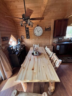 A wooden dining table with chairs, a clock, and a ceiling fan in a cabin-style room. - Family friendly 3-bedroom cabin in peaceful Vanderbilt. Private. Large groups. (Vanderbilt)